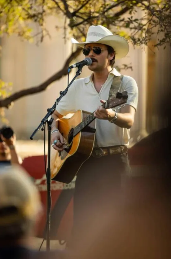 Man with cowboy hat standing playing acoustic guitar in front of a mic